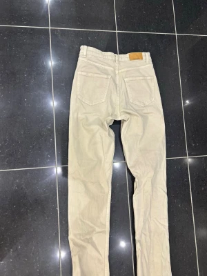 Beiga raka jeans med rå kant - Säljer ett par beiga jeans med raka ben och råa, fransiga benslut. Jeansen har två bakfickor och är tillverkade i ett klassiskt denimtyg. Perfekta för en avslappnad och trendig look.