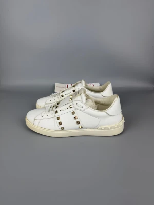 Valentino Open Rockstud Untitled Sneaker White | 42 - Vita sneakers i läder med guldfärgade nitar. Mycket gott skick, storlek 42.