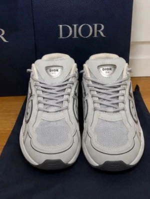 Grå Dior B30  sneakers i mesh och läder - Snygga grå sneakers från Dior med coola detaljer i mesh och läder. Skorna har en chunky sula, snörning framtill och CD-logga på hälen. Perfekta för dig som vill ha en exklusiv och trendig look.