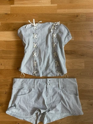 Randigt set med snörning - Säljer ett tvådelat set med topp och shorts i vitt och grått med tunna ränder. Toppen har dekorativ snörning. Aldrig använd och köpt på Zara