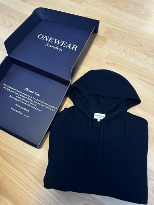 Kashmir Hoodie - Storlek S. 100% Kashmir. Original pris 1299 kr. En stilren marinblå hoodie från ONEWear Sweden med klassisk huva och dragsnören. Hoodien har långa ärmar och ribbade muddar vid ärmslut och nederkant. Perfekt för dig som gillar enkel och clean stil. Materialet känns mjukt och bekvämt. OBS! Ett litet hål i armhålan på högersida men syns inte vid användning. (Se sista bilden)