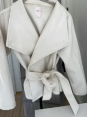 Vit kappa från Gina Tricot (helt ny)! - Stilren vit kappa från Gina Tricot i storlek XXS. Kappan har breda slag, knytskärp i midjan och raka ärmar. Perfekt för hösten! storleken är som en xs på, den är i nyskick inga fläckar! 