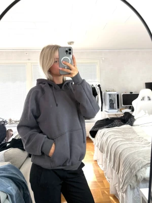 Mörkgrå oversized hoodie - Säljer en mörkgrå oversized hoodie med huva och känguruficka framtill. Hoodien har långa ärmar, ribbade muddar och en avslappnad passform. Perfekt för dig som gillar en enkel och stilren look.