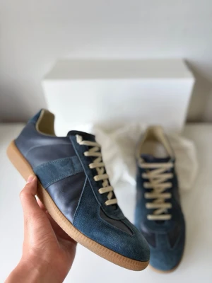 Maison margiela gats - Snygga sneakers i blå mocka och läder med beige snörning och gummisula. Skorna har en klassisk låg silhuett och stilrena detaljer som passar till många outfits. Perfekta för dig som gillar en clean och modern look.