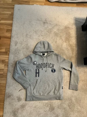 Grå hoodie från Hoodrich med tryck - Pris diskuteras privat!! Säljer en grå hoodie från Hoodrich med tryck och patchar på bröstet. Hoodien har huva med dragsko, magficka och ribbade muddar vid ärmslut och nederkant. Perfekt för en avslappnad streetwear-look.