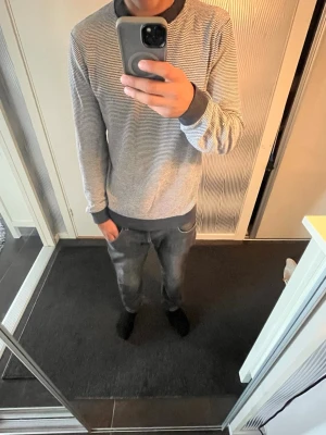 Randig grå sweatshirt från Jack&Jones - Säljer en stilren grå sweatshirt med tunna svarta ränder och svarta muddar vid ärmslut, halsringning och nederkant. Tröjan har en avslappnad passform och är perfekt för dig som gillar en enkel men snygg look.
