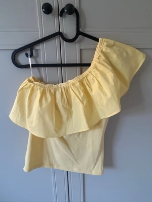 Gul oneshoulder topp  - Super söt gul volang topp som aldrig kommer till användning! Är i storlek 158/164 och passar mig som har xs!