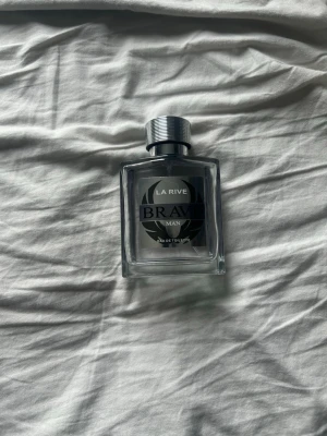 La Rive Brave Man Eau de Toilette - La Rive Brave Man Eau de Toilette är en parfym för män i en stilren, fyrkantig glasflaska med silverfärgat metallock. Flaskan har en svart och silver etikett med modern design. Perfekt för dig som gillar maskulina och fräscha dofter.