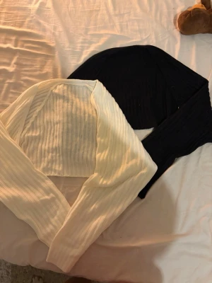 Två ribbade boleros i svart och vitt - Säljer två stilrena boleros i ribbat material, en i svart och en i vitt. Båda har lång ärm och är perfekta att slänga över ett linne eller topp för en trendig lager-på-lager-look. Materialet är stretchigt och följsamt.