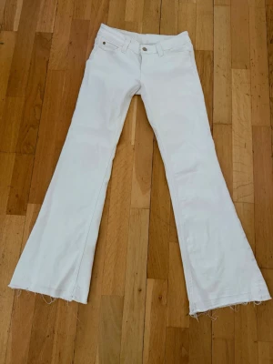 Vita utsvängda jeans med rå kant - Säljer ett par vita jeans med utsvängda ben och råa, fransiga benslut. Jeansen har klassisk femficksmodell och bälteshällor. Perfekta för dig som vill ha en retro och trendig look. Materialet känns som bomull med bra strech. 