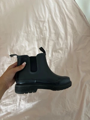 Svarta Chelsea boots i gummi- Ilse Jacobsen  - Säljer ett par svarta Chelsea boots i gummi från klädesmärket Ilse Jackobsen,  elastiska paneler på sidorna och dragflikar både fram och bak. Mycket bra skick, använda enstaka gånger och ligger ute orginalpris mellan 1500-2000 kr . 