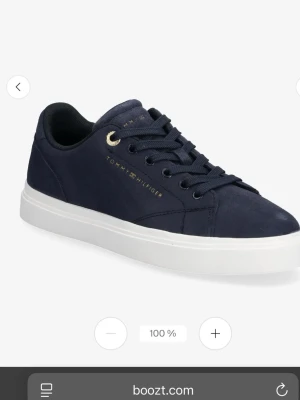 Mörkblå sneakers Tommy Hilfiger - Stilrena mörkblå sneakers från Tommy Hilfiger med vit sula och gulddetaljer vid snörningen. Skon har en klassisk låg profil och är tillverkad i mockaliknande material med diskret logga på sidan. Perfekt för dig som gillar en clean och modern look.