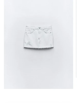 Vit jeanskjol med fransig kant - Säljer en vit kort jeanskjol med slitna detaljer och fransig rå kant nedtill. Kjolen har klassiska fem fickor och knappgylf. Perfekt för dig som gillar en avslappnad och trendig stil.