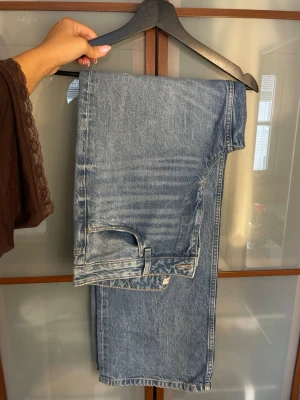 Blå raka jeans från Gina Tricot - Ett par klassiska blå jeans från Gina Tricot med rak passform och hög midja. Jeansen har fem fickor, bälteshällor och en ljus tvättad denimlook. Perfekta för en avslappnad och trendig stil.