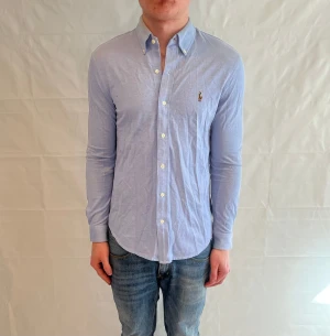 Polo Ralph Lauren Knit Oxford Shirt Light Blue - Ljusblå skjorta i 100% bomull. Begagnad i fint skick, med lätt missfärgning vid kragen.