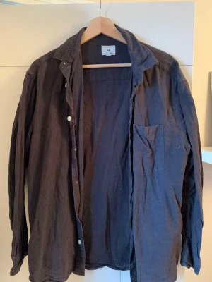 Svart linneskjorta från H&M - Säljer en svart linneskjorta från H&M i relaxed fit. Skrynklor försvinner efter strykning. Skjortan har långa ärmar, klassisk krage, bröstficka och knäppning framtill. Perfekt för en chill och stilren look. Materialet är mjukt och skönt linnetyg.