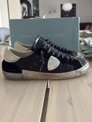 Philippe Model svarta sneakers - Svarta Philippe Model sneakers med vita detaljer och logga på sidan. Skorna har lågt skaft, svarta skosnören och en vit sula med sliten look. Materialmix av läder och mocka ger en schysst kontrast. Perfekta för dig som gillar streetstyle. Inga defekter på skorna! Hör av dig vid frågor om skorna! Priset går att diskutera