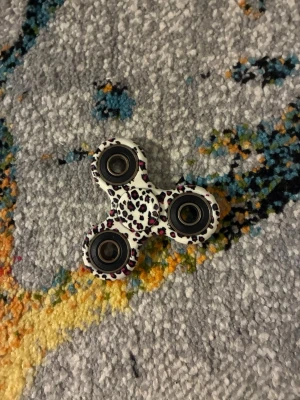Fidget spinner med leopardmönster - En fidget spinner i plast med vitt, svart och lila leopardmönster. Spinnern har tre armar med metallkullager i varje ände och är perfekt för att hålla händerna sysselsatta eller för att slappna av.