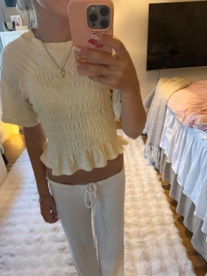 Ljusgul smockad topp Gina Tricot - Supersöt ljusgul topp från Gina Tricot i smockat tyg med korta ärmar och volangkant nedtill. Toppen har en croppad passform och är gjord i mjuk bomull, perfekt för en fräsch och trendig look.
