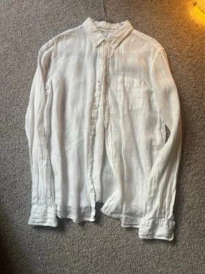 Vit linneskjorta från Gant - Nypris ca 1000kr Klassisk vit skjorta i linne från Gant med bröstficka och knappar framtill. Skjortan har lång ärm, krage och en avslappnad passform. Perfekt för en stilren och enkel look.