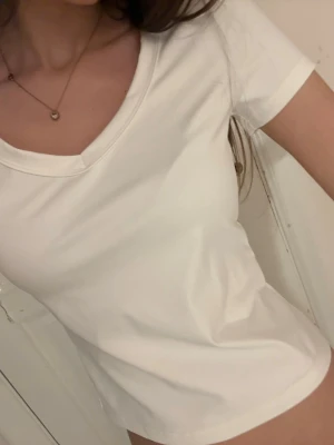 Vit v-ringad t-shirt - En enkel och fräsch vit t-shirt med v-ringning och korta ärmar. T-shirten har en klassisk passform och är gjord i mjukt bomullstyg som känns skönt mot huden. Perfekt till jeans eller kjol för en clean look.