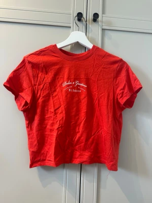 Röd croppad t-shirt från H&M - Snygg röd croppad t-shirt från H&M Divided med tryck framtill. Aldrig använd!