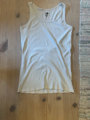 Vit ribbad linnetopp från H&M - Klassisk vit ribbad linnetopp från H&M med rundad halsringning och smala axelband. Tillverkad i mjuk bomull som sitter skönt mot kroppen. Perfekt att matcha till kjol eller jeans för en enkel och fräsch stil.
