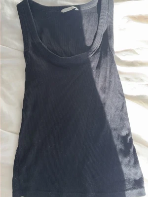 Svart ribbad linnetopp från Zara - Säljer en svart ribbad linnetopp från Zara. Toppen är ärmlös med rund halsringning och har en tight passform. Perfekt att styla till jeans eller kjol för en enkel och clean look.