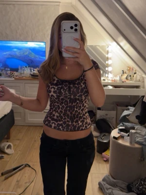 Leopardmönstrad croppad topp - Snygg croppad topp med leopardmönster och korta ärmar. Toppen har en lätt åtsittande passform och en liten rosettdetalj framtill vid halsringningen. 