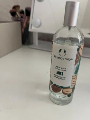 The Body Shop Shea Body Mist - Fräsch body mist från The Body Shop med sheadoft. Kommer i en genomskinlig glasflaska med silverfärgad spraykork och dekorativt mönster med nötmotiv. Vegansk formula och innehåller 97% ingredienser av naturligt ursprung. Perfekt för en uppfriskande känsla. 