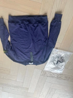 Mörkblå sweatshirt från Stone Island - Mörkblå sweatshirt från Stone Island med klassisk rund halsringning och ribbade muddar. Tröjan har den ikoniska Stone Island-loggan på vänster ärm och är tillverkad i mjuk bomull. Perfekt för en avslappnad och stilren look. Passar även S