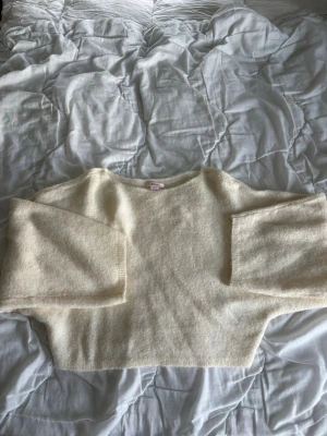 Krämvit oversized stickad tröja - Mysig krämvit stickad tröja med bred passform och långa, vida ärmar. Tröjan har en enkel, rak design och är tillverkad i ett mjukt, fluffigt material som känns skönt mot huden. Perfekt för lager på lager och en avslappnad look.