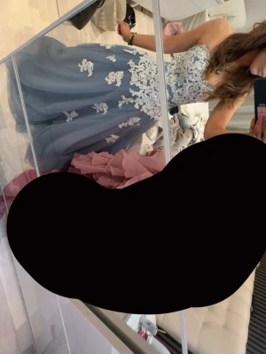Balklänning - Säljer en blå balklänning med vita spetsapplikationer och axelbandslös design. Klänningen har en vid kjol i tyll och vacker v-ringad överdel med blommiga spetsdetaljer. Perfekt för bal eller festliga tillfällen. Ny pris 6000kr använd en gång!! Skriv vid frågor