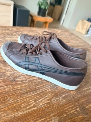 onitsuka tiger bruna skor  - Snygga bruna sneakers i lågt snitt med svarta detaljer på sidorna och vita sulor med röd undersida. Skorna har klassisk snörning och är tillverkade i ett material som ser ut som läder. Perfekta för en avslappnad och stilren look.