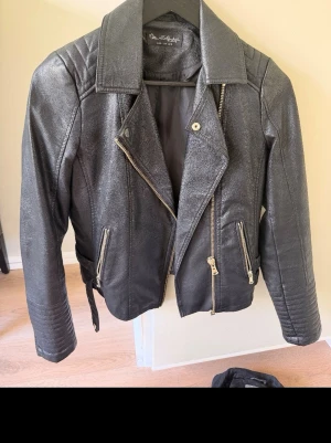 Svart skinnjacka från Miss Selfridge - Snygg svart skinnjacka från Miss Selfridge i klassisk bikerstil med bred krage, sneddraget blixtlås och detaljerade dragkedjor på fickorna. Jackan har en cool, kortare passform och markerade axlar som ger en edgy look.