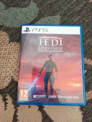 Star Wars Jedi Survivor PS5 spel - Star Wars Jedi Survivor till PS5 i blå plastfodral. Omslaget visar huvudkaraktären med ett blått ljussvärd mot en röd och orange himmel. Spelet är från Electronic Arts och har PEGI 12-märkning. Perfekt för dig som gillar action och äventyr i Star Wars-universumet.