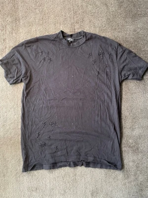 MAN T-shirt – Svart Distressed - Snygg svart t-shirt från MAN med distressed-detaljer.  ✅ Svart bomullstyg ✅ Distressed-hål utspridda över tröjan – del av designen ✅ Rund halsringning ✅ Korta ärmar ✅ Storlek M men passar L/XL  En cool basic med attityd, perfekt för dig som gillar en trasig/street-inspirerad stil. Skriv gärna vid frågor eller för fler bilder!