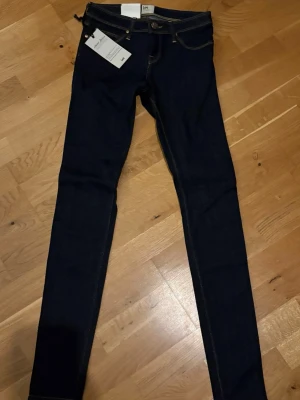 Mörkblå skinny jeans från Lee - Snygga mörkblå skinny jeans från Lee med klassisk femficksmodell och kontrastsömmar. Jeansen har smal passform hela vägen ner. Ej en stretchig modell. Perfekta för dig som gillar en slimmad look. Storlek: W25, L33, helt nya och endast förvarats i garderoben ✨