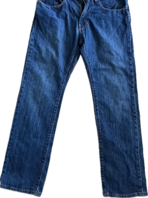 Blå raka jeans i klassisk modell - Säljer ett par blå jeans med rak passform och fem fickor. Jeansen har normal midja och är tillverkade i slitstark denim. Perfekta för dig som gillar en tidlös och enkel stil. Passar till det mesta och är ett måste i garderoben.