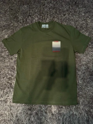 Grön Casa Blanca t-shirt - Snygg grön t-shirt från Casa Blanca med tryck i vitt och rött på bröstet och ryggen. Perfekt för dig som vill ha en stilren men ändå unik look.  Tags och påse finns också 