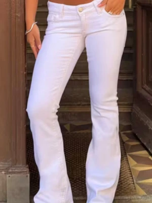 Vita bootcut jeans med låg midja - Säljer ett par vita bootcut jeans med låg midja och klassisk femficksmodell. Jeansen har en snygg utsvängd passform och stängs med knapp och dragkedja. Perfekta till sommaren och lätta att matcha med olika stilar. Passar nån runt 160-165