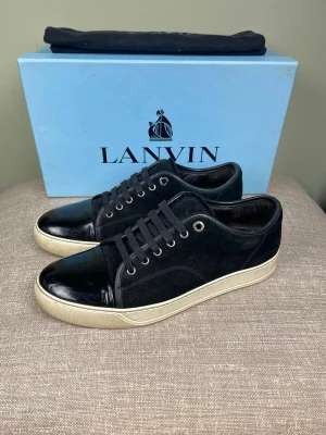 Lanvin skor - Snygga svarta sneakers från Lanvin med ovandel i mocka och lackad tå. Skorna har vita sulor och svarta skosnören. Perfekta för dig som gillar stilrena och exklusiva sneakers med en twist.