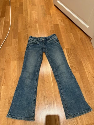 Blå bootcut jeans med låg midja - Säljer ett par klassiska blå bootcut jeans med låg midja. Jeansen har en snygg tvättad look och är i ett mjukt denimtyg som sitter skönt. Perfekta för dig som gillar lite basic men även en extra touch på fickorna. 