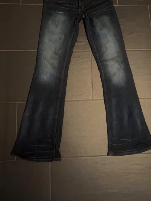 Mörkblå bootcut jeans med slitningar - Säljer ett par mörkblå bootcut jeans med snygga slitningar framtill. Jeansen har klassisk femficksmodell och utsvängda ben. Perfekta för dig som gillar en retro och avslappnad stil. Jeans ifrån cheap Monday aldrig använda säljer då jag köpte fel storlek.  Storlek 32/34