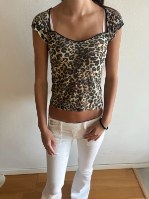 Leopardmönstrad croppad topp - Snygg croppad topp med leopardmönster och korta ärmar. Toppen har en lätt v-ringad halsringning med svarta detaljer längs kanten. Perfekt för dig som vill sticka ut och addera lite edge till din outfit.