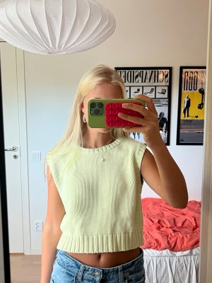 Ljusgul stickad ärmlös tröja - Ljusgul stickad väst i en grön ton💛💚 Tröjan har ribbad kant vid halsringningen, ärmhål och nederkant och är croppad i modellen. Jättefin att styla över en skjorta eller t-shirt! Materialet är bomull och akryl.