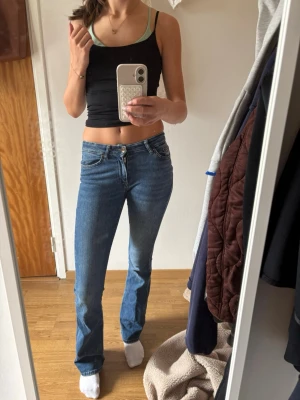 Blå raka jeans med hög midja - Säljer ett par klassiska blå jeans med rak passform och mid/Low waist . Jeansen har fem fickor, bälteshällor och stängs med dragkedja och knapp. Perfekta till en enkel topp eller hoodie för en avslappnad look.