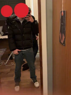 Svart pufferjacka från Burberry S - Säljer en svart pufferjacka från Burberry med klassiskt rutigt foder i huvan och diskret logga på ärmen. Jackan har dragkedja, stora vadderade partier och praktisk huva. Perfekt för kalla vinterdagar och riktigt snygg streetstil.
