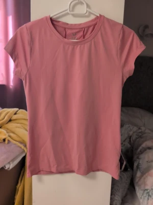 Rosa tränings-tshirt från SOC - Säljer en rosa tränings-tshirt från SOC i funktionsmaterial. T-shirten har rund halsringning och korta ärmar, perfekt för gymmet eller löprundan. Materialet är lätt och andas, vilket gör den skön att bära under träning.