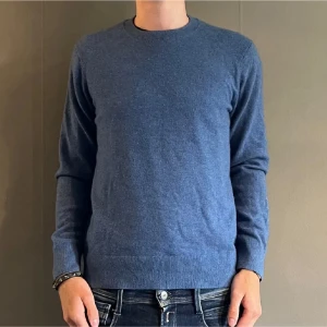 Kashmir tröja - En stilren blå stickad tröja med rund halsringning och långa ärmar. Tröjan har ribbade muddar vid ärmslut och nederkant. Perfekt för lager på lager och enkel att matcha med jeans eller chinos. Materialet känns mjukt och värmande.